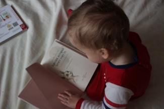 baby sitting on bed while reading on book by Iana Dmytrenko courtesy of Unsplash.